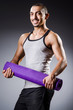 Muscular man with mat in studio