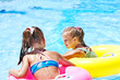 Children sitting on inflatable ring in water.