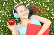 Young female listening music and holding an apple, on a green gr