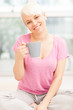 Smiling woman with mug sitting at home while smiling