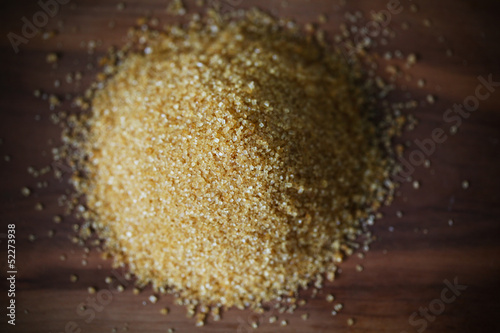 Photo: Brown sugar from cane, crystals in heap on brown wooden board Brown sugar from cane, crystals in heap on brown wooden board