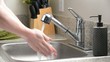 Man washes hands in kitchen sink and dries with green towel