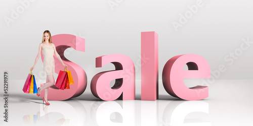 Photo: Young woman with shopping bags standing next to a word SALE Young woman with shopping bags standing next to a word SALE