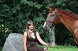 Beautiful teenage girl resting on the rock in park and horse sta