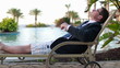 Happy businessman relaxing on sunbed by the swimming pool