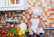 Foto: Baby cook with vegetables sits on a kitchen table Baby cook with vegetables sits on a kitchen table