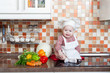 Foto: Baby cook with vegetables sits on a kitchen table Baby cook with vegetables sits on a kitchen table