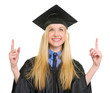 Happy young woman in graduation gown pointing up on copy space