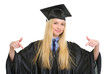 Happy young woman in graduation gown pointing down on copy space
