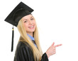 Smiling young woman in graduation gown pointing on copy space