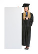Happy young woman in graduation gown pointing on blank billboard