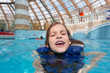 Photo: Happy girl in lifejacket in the clear blue water in water park. Happy girl in lifejacket in the clear blue water in water park.