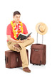 Male tourist sitting on a briefcase and reading a book