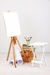 Wooden easel with clean paper and art supplies in room