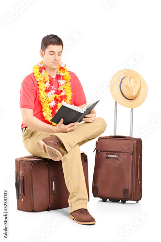 Photo: Male tourist sitting on a briefcase and reading a book Male tourist sitting on a briefcase and reading a book