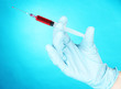 Hand holding syringe filled with blood on blue background
