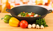 Wok with vegetable ragout on wooden table, on bright background