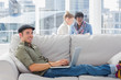 Smiling worker using his laptop while laying on a couch