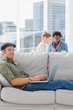 Cheerful worker using his laptop while laying on a couch