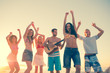 Group of friends having fun on the beach and playing guitar