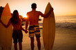 Couple hand in hand holding surfboards