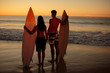 Couple hand in hand holding surfboards on the beach