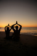 Silhouettes of people practicing yoga sat on the sand