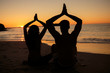 Silhouettes of people practicing yoga sat on the beach