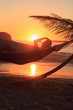 A person wearing a straw hat and relaxing in hammock on the beach