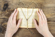 Hands holding the Bible and praying with a rosary