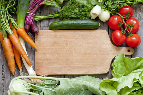 Photo: Many fresh organic vegetables and empty cutting board background Many fresh organic vegetables and empty cutting board background