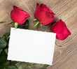 three red roses and blank sheet on wood