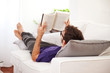 Young man stretching comfortably on couch and reading a book