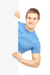 Casual young man posing behind white panel