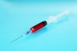Plastic disposable syringe filled with blood on blue background