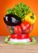 Fresh vegetables in scales on table on orange background