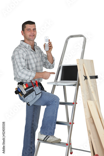 Photo: Carpenter standing by a ladder with a mobile telephone Carpenter standing by a ladder with a mobile telephone