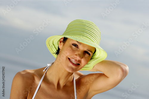 Photo: Brunette holding on to her hat at the beach Brunette holding on to her hat at the beach