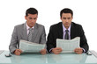 Two businessman sat with newspapers
