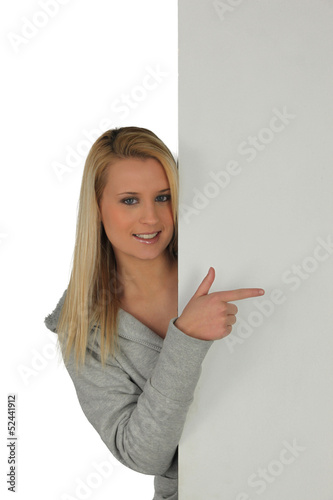 Photo: Blond girl pointing at blank panel Blond girl pointing at blank panel
