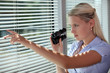 woman looking through the blinds with binoculars