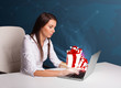 Photo: Pretty lady sitting at desk and typing on laptop with present bo Pretty lady sitting at desk and typing on laptop with present bo