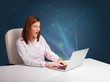 Photo: Beautiful woman sitting at desk and typing on laptop with abstra Beautiful woman sitting at desk and typing on laptop with abstra