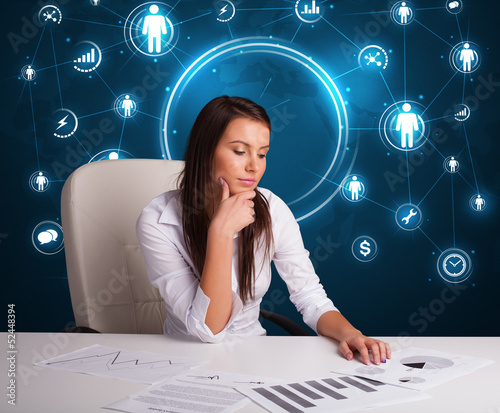 Photo: Businesswoman sitting at desk with social network icons Businesswoman sitting at desk with social network icons