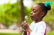 Foto: Outdoor portrait of a cute young black girl blowing a dandelion Outdoor portrait of a cute young black girl blowing a dandelion