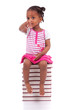 Photo: Cute black african american little girl seated in a stack of boo Cute black african american little girl seated in a stack of boo