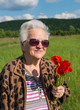 Elderly woman in sunglasses with bunch of poppies
