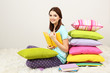 Photo: Beautiful young girl with pillows and books in room Beautiful young girl with pillows and books in room