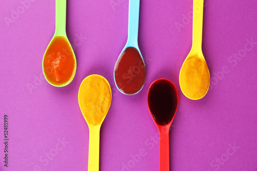 Photo: Baby puree in spoons on purple background Baby puree in spoons on purple background