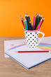Colorful pencils in cup on table on orange background